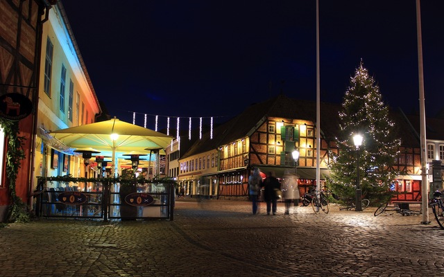Beleuchteter Platz mit Fachwerkhäusern und Weihnachtsbaum bei Nacht.