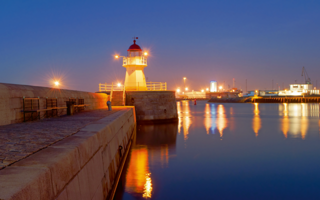Ein beleuchteter Leuchtturm bei Abenddämmerung am Hafen.