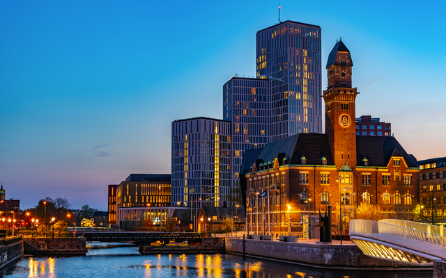 Stadtsilhouette mit modernen und historischen Gebäuden bei Sonnenuntergang entlang eines Kanals