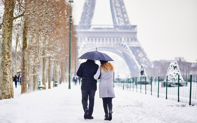 Paar unter Regenschirm im Schnee vor dem Eiffelturm in Paris.