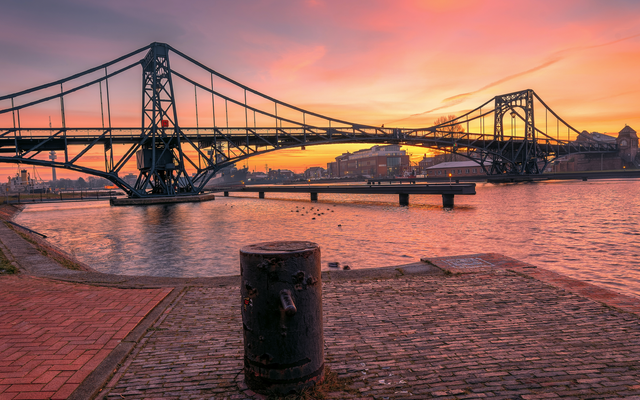 Brücke über einem Fluss bei Sonnenuntergang mit wolkigem Himmel.