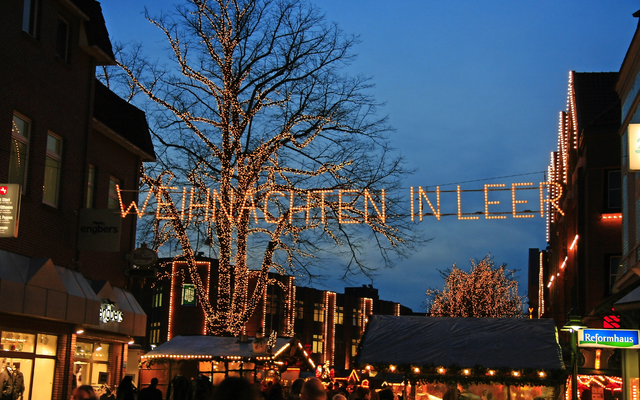 Weihnachtsmarkt mit Lichterdekoration und Baum in der Abenddämmerung.
