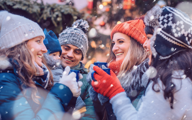 Gruppe von Menschen in Winterkleidung trinkt heiße Getränke im Freien.