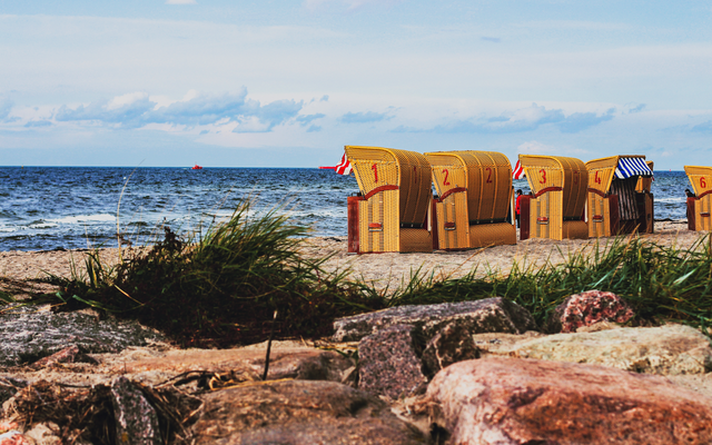 Strandkörbe am Sandstrand vor der Ostsee mit Wolkenhimmel im Hintergrund.