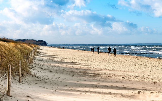 Menschen spazieren an einem sonnigen Sandstrand entlang der Küste.