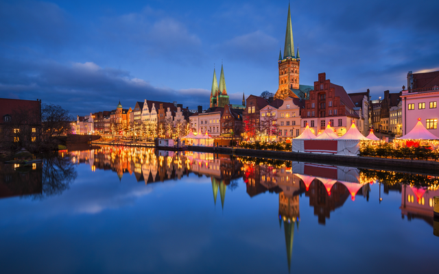Altstadt mit beleuchtetem Weihnachtsmarkt am Flussufer bei Abenddämmerung.