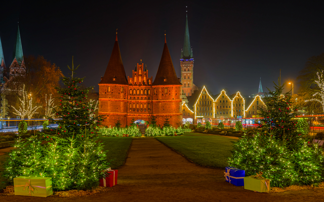 Weihnachtsmarkt vor beleuchtetem Holstentor in Lübeck bei Nacht