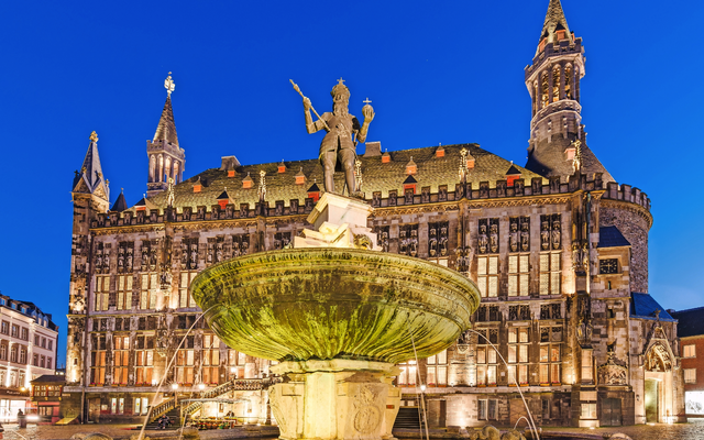 Historisches Gebäude mit Brunnen bei Nacht im Hintergrund illuminierter Himmel.