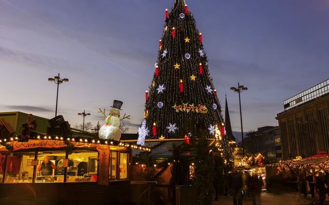 Weihnachtsmarkt mit beleuchtetem Baum und Verkaufsständen bei Abenddämmerung.