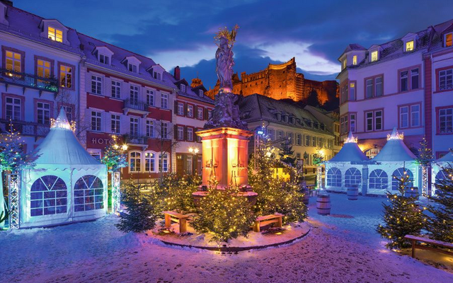 Beleuchteter Weihnachtsmarkt bei Schneefall in historischer Altstadt mit Festzelten