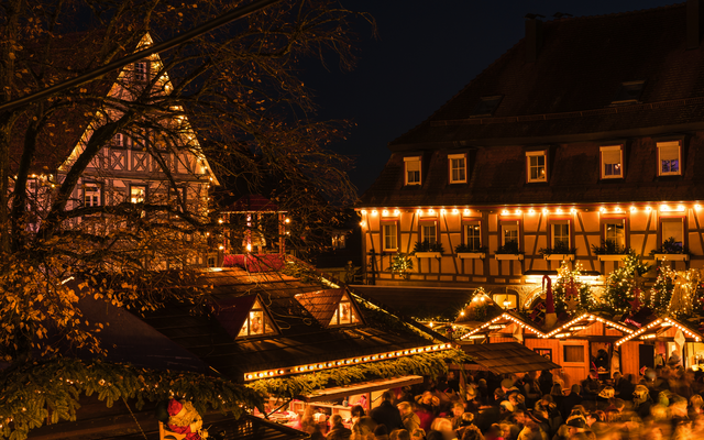 Abendlicher Weihnachtsmarkt mit Fachwerkhäusern und Lichterdekoration.