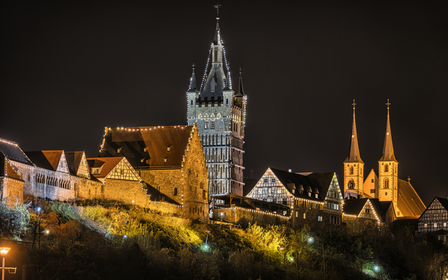 Beleuchteter Schlosskomplex bei Nacht mit Türmen und Fachwerkhäusern.