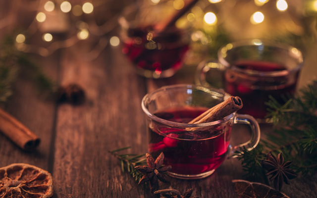 Zwei Gläser Glühwein mit Zimtstangen auf einem Holztisch, umgeben von Tannenzweigen.
