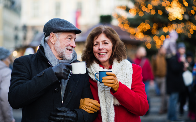 Älteres Paar trinkt Heißgetränke auf einem Weihnachtsmarkt.