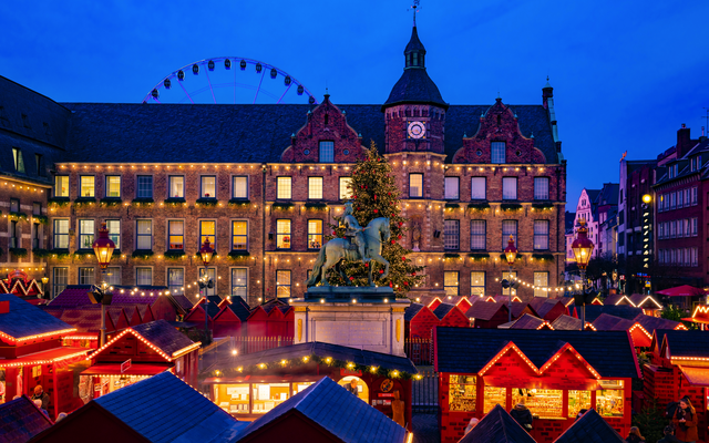 Weihnachtsmarkt mit beleuchtetem Gebäude und Statue in der Abenddämmerung
