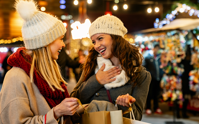 Zwei lachende Frauen mit Einkaufstaschen auf einem Weihnachtsmarkt.