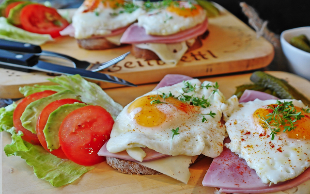 Sandwich mit Schinken, Spiegelei, Tomaten und Salat auf Holzbrett.