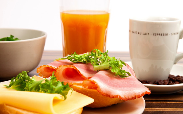 Frühstück mit einem belegten Brötchen, Kaffee und Saft.