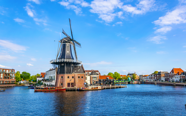 Windmühle am Wasser mit umliegenden Gebäuden und blauem Himmel.
