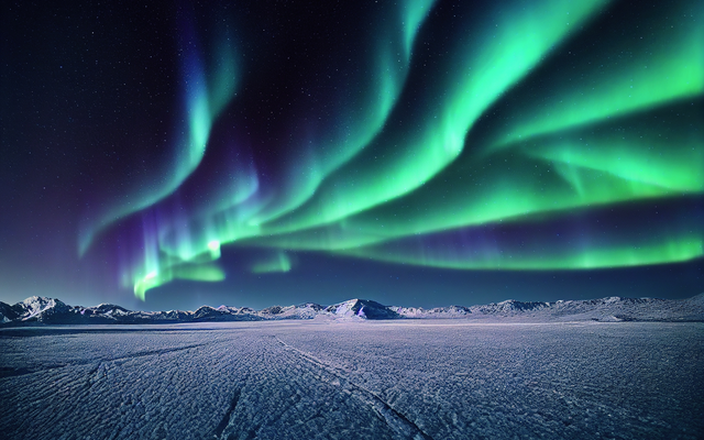 Polarlichter über einer verschneiten und vereisten Landschaft in Norwegen.