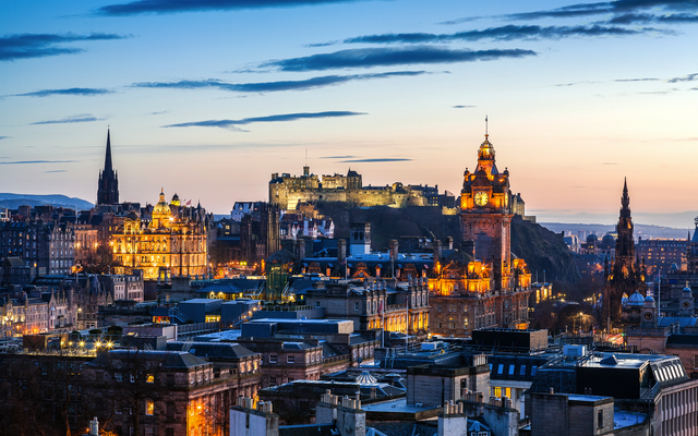 Blick auf Edinburgh zur Dämmerung im Winter, beleuchtete Stadt mit der Burg im Hintergrund.