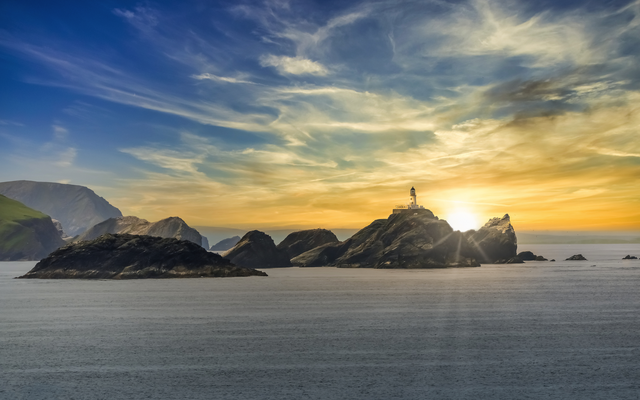Leuchtturm auf Felsen im Meer bei Sonnenuntergang, umgeben von Wasser und Himmel.