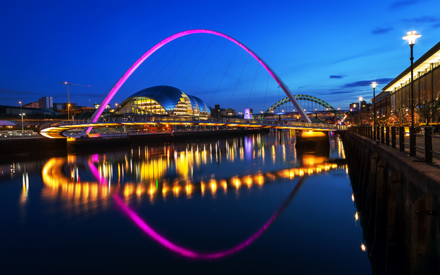 Flusslandschaft mit beleuchteter Brücke und Stadt bei Nacht.