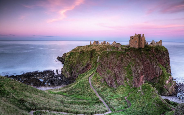 Ruinen von Dunnottar Castle auf einer Klippe bei Sonnenuntergang, umgeben von Meer.