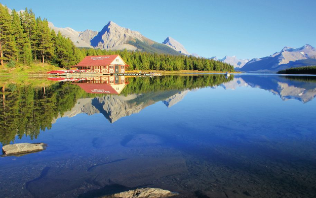 Berglandschaft mit See und Hütte im Vordergrund, klare Spiegelung im Wasser.
