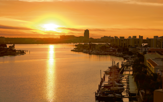 Sonnenuntergang über einem Fluss mit Yachthafen und Stadtansicht im Hintergrund.