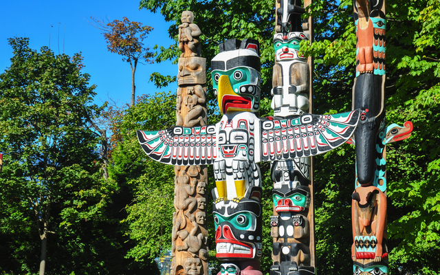 Verschiedene farbenfrohe Totempfähle im Stanley Park in Vancouver, umgeben von grünen Bäumen.
