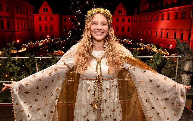 Frau in Weihnachtsengel-Kostüm vor beleuchteter Schlosskulisse bei Nacht.