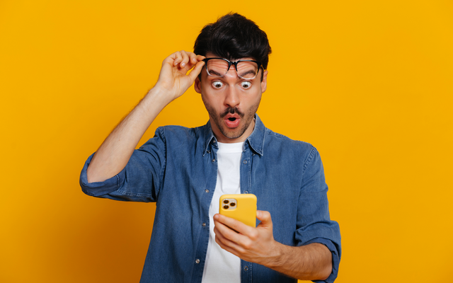 Ein Mann mit Brille schaut überrascht auf ein Smartphone, isolierter Hintergrund.