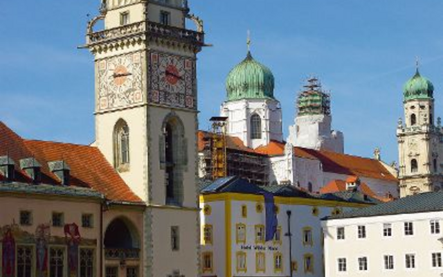Rathausturm in Passau mit angrenzenden Gebäuden am Flussufer, blauer Himmel im Hintergrund.