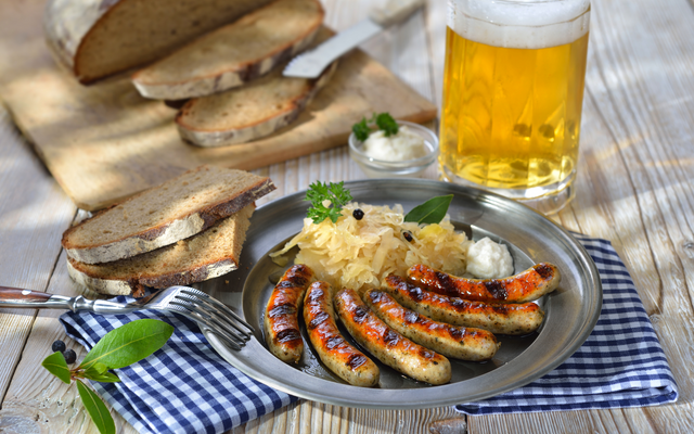 Teller mit Bratwürsten, Sauerkraut und Brot, dazu ein Glas Bier.