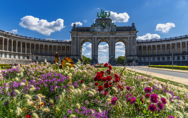 Blumenbeet vor dem Triumphbogen im Park mit blauem Himmel und Wolken.