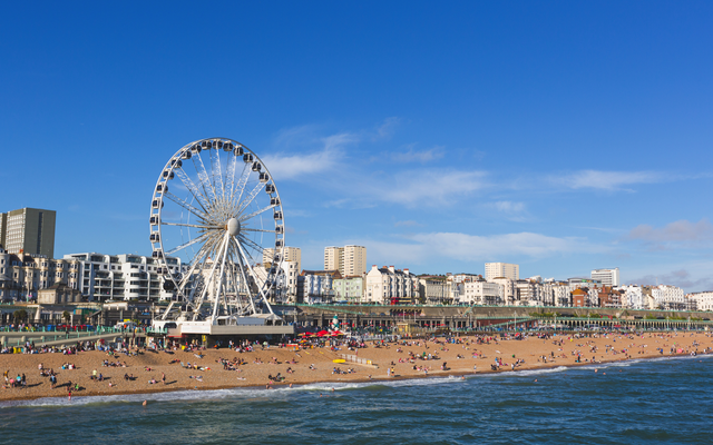 Riesenrad am Strand vor städtischer Kulisse bei klarem Himmel.