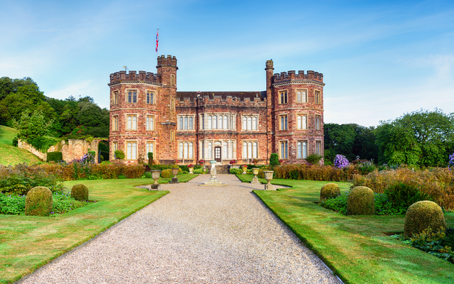Altes Schloss mit Garten und blauen Himmel im Hintergrund.