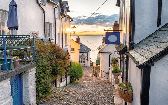 Steile gepflasterte Gasse mit weißen Häuschen und Blick auf das Meer bei Sonnenuntergang.