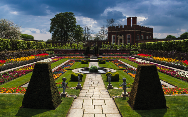 Formale Gartenanlage mit symmetrischen Blumenbeeten und einem Herrenhaus im Hintergrund.