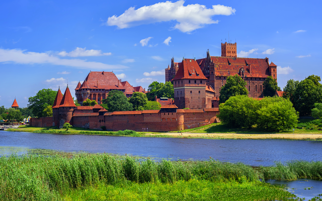 Burg auf Hügel am Flussufer unter blauem Himmel mit Wolken.