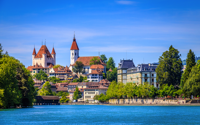 Stadtansicht mit Schloss, Kirche und Fluss bei blauem Himmel.