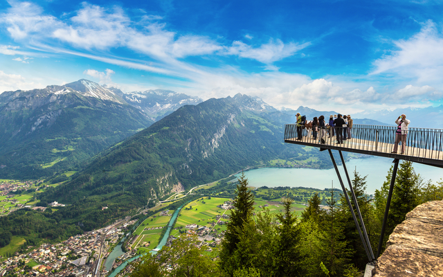 Aussichtspunkt mit Menschen, Blick auf Berglandschaft und See im Hintergrund.