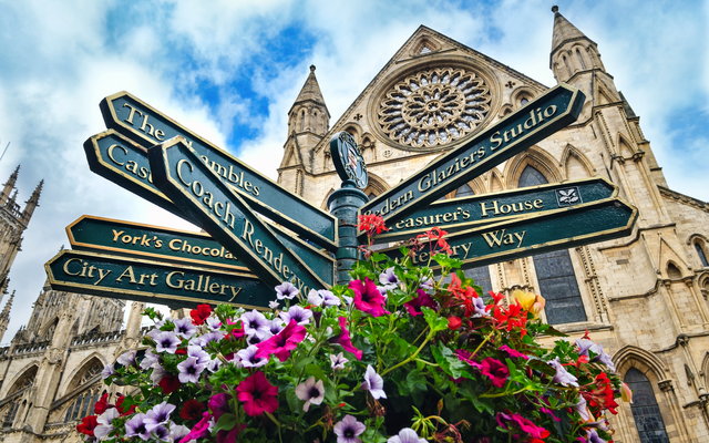 Wegweiser vor gotischer Kathedrale in York, umgeben von Blumen.