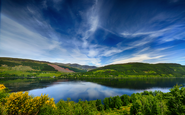 Landschaft mit See, Wäldern und Wolken am Himmel.