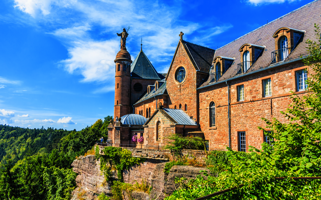 Historisches Schloss auf Felsvorsprung mit Turm und blauer Himmel im Hintergrund.