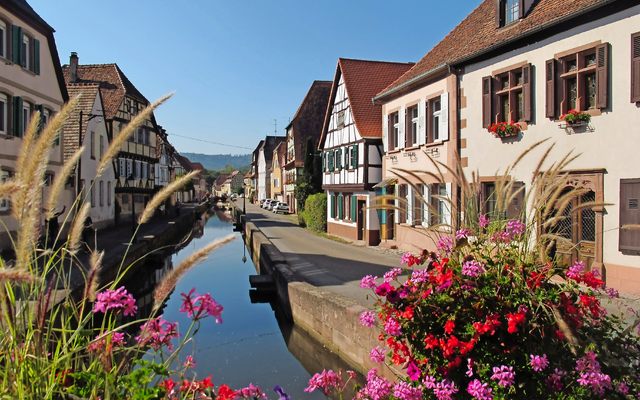 Kanal und Fachwerkhäuser in einer malerischen Stadt mit Blumen im Vordergrund.