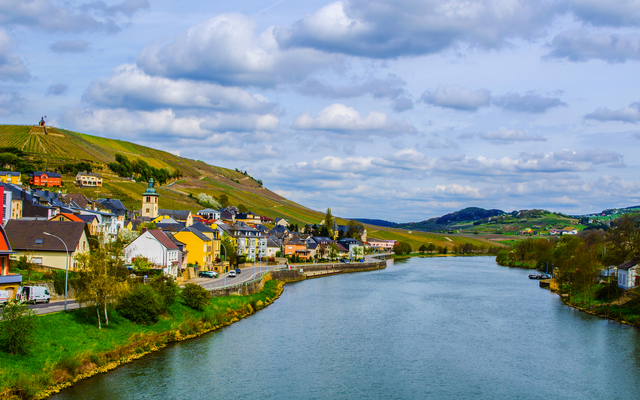 Flusslandschaft mit einer Stadt und Weinbergen im Hintergrund.