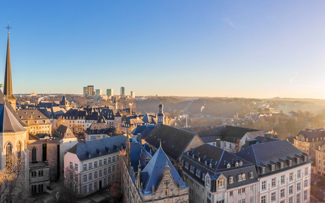Panorama von Luxemburg-Stadt bei Sonnenuntergang mit Kirchendach und Altstadtgebäuden.
