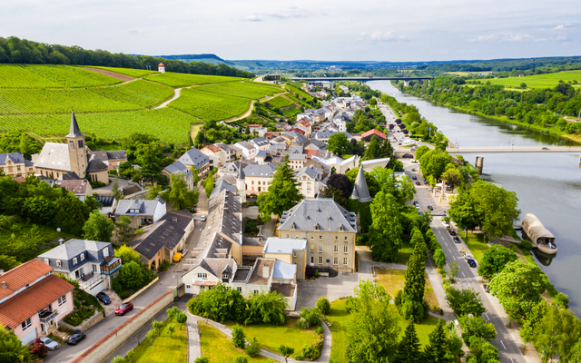 Luftaufnahme eines Dorfes mit Kirche, Fluss und Weinanbaugebieten.